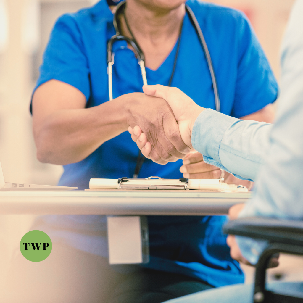 A healthcare professional in blue scrubs shaking hands with a patient in a clinical setting, representing the trust and care in healthcare services, accompanied by the TWP logo.